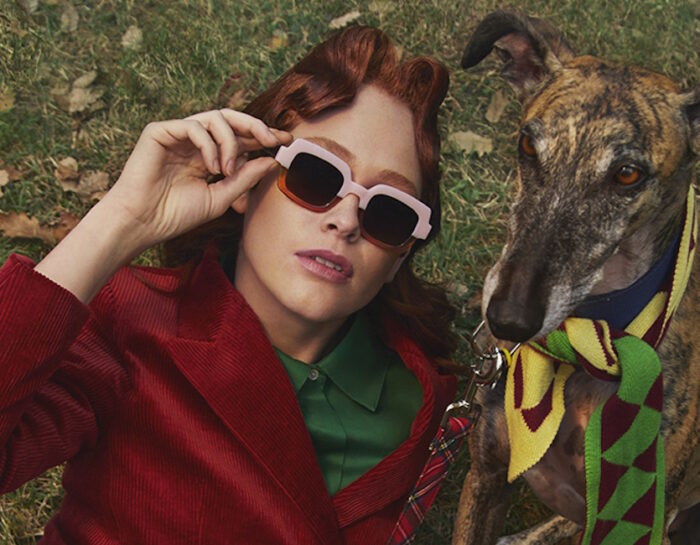 Une femme allongée dans l'herbe avec son chien porte des lunettes de soleil de la marque espagnole Woodys.