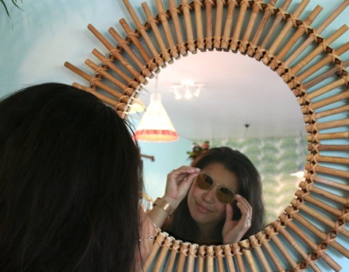 Une femme sourit et se regarde dans un miroir décoré comme un soleil