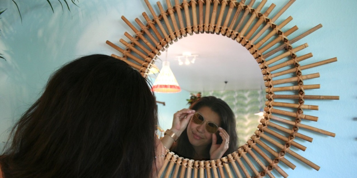 Une femme sourit et se regarde dans un miroir décoré comme un soleil