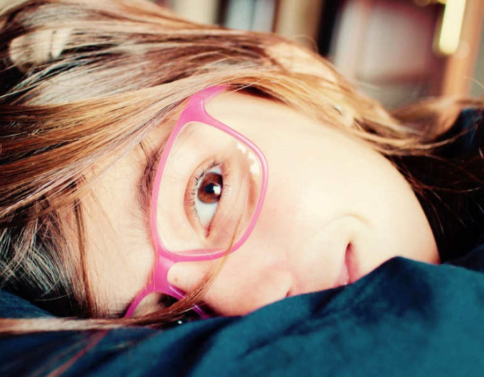 jeune fille portant des lunettes roses allongée dans des draps et sourit