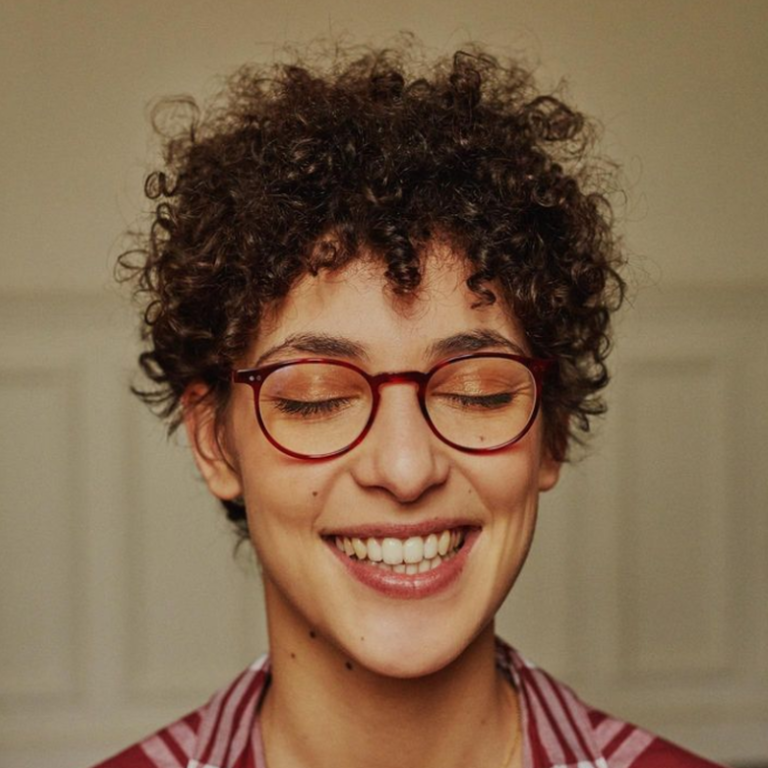 photo de campagne pour les lunettes de la marque Tortuga. Une femme, les yeux fermés et un grand sourire porte de jolies lunettes ronde rouge vintage
