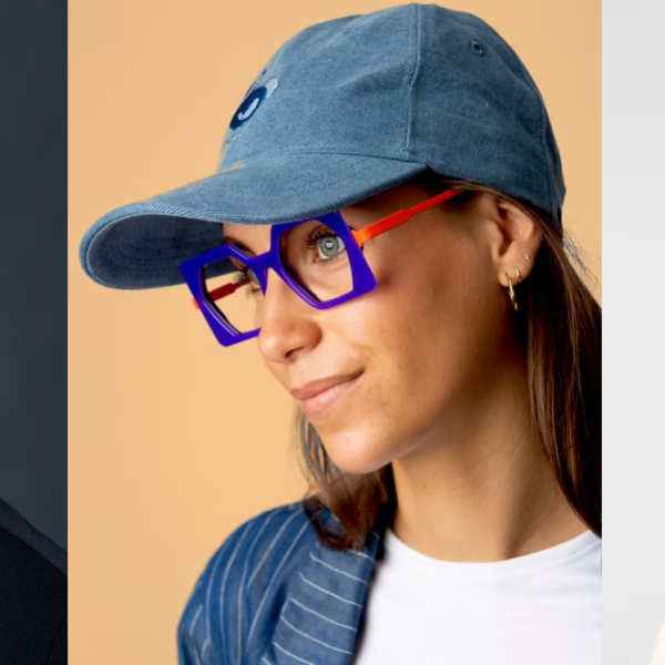 Une femme souriante qui porte une casquette sur la tete. Porte les jolies lunettes bleue et orange de la marque la brique et la voilette